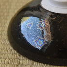 Close-up underside detail of the Touan matcha bowl highlighting colorful star-like Hoshi-Kessho crystal formations in the glossy black glaze