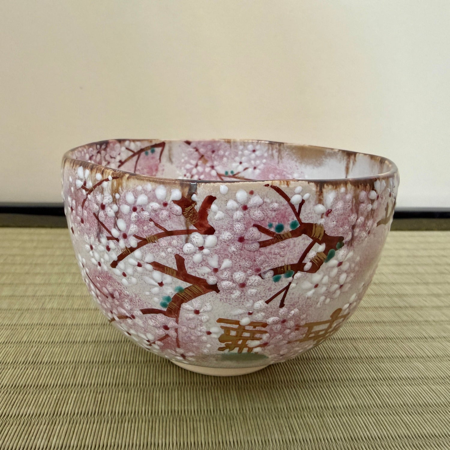 Side view of the hand-painted chawan showing layered pink sakura blossoms, dark branches, and the Togetsukyo Bridge landscape wrapping around the exterior.