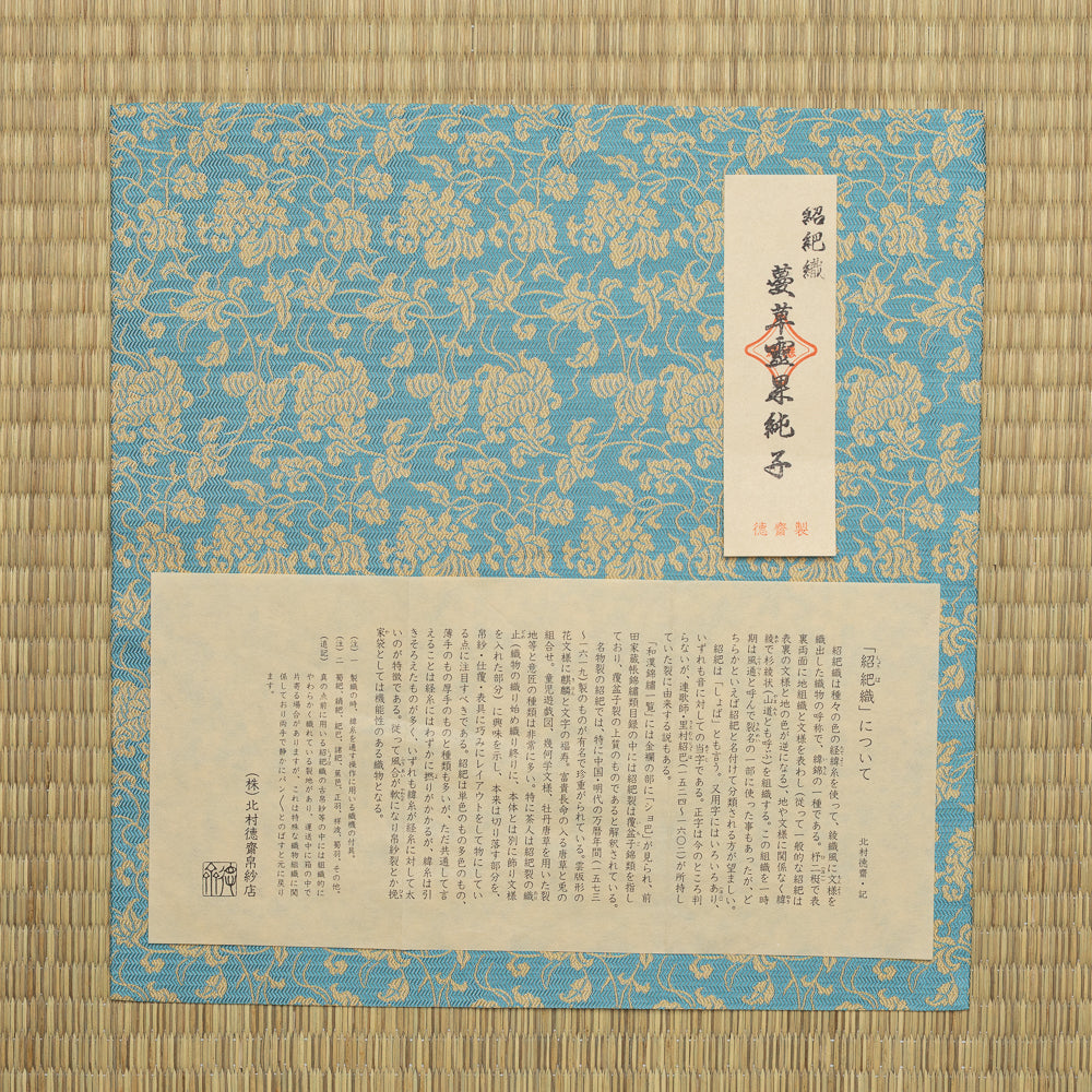 Close-up of scrolling vines and stylized floral motifs woven in gold-toned silk on a turquoise-blue ground.