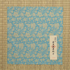 Turquoise-blue silk dashibukusa displayed with its Japanese maker label and product information card.