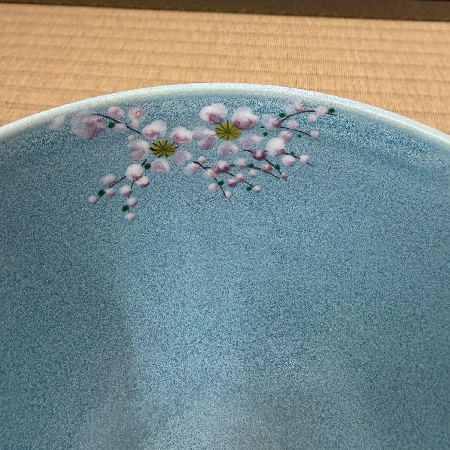Close-up of the turquoise matcha bowl showing delicate pink and white cherry blossoms with green details near the rim.