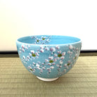 Front angled view of the Kato Eizan chawan showing weeping sakura branches flowing across the luminous turquoise exterior.