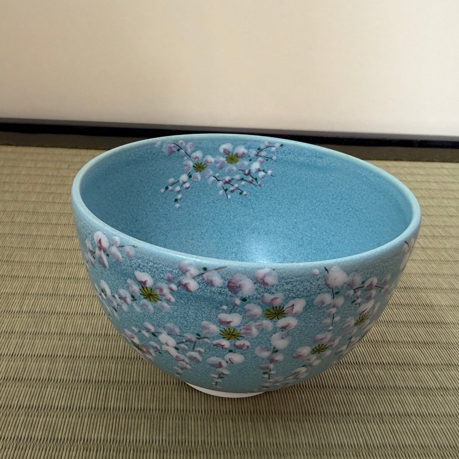 Angled top view of the turquoise Kyo Ware matcha bowl showing its blue-green interior and cherry blossom decoration continuing over the rim.