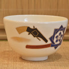 Right-side view of the hand-painted Kyo Ware bowl with pistol imagery, layered blue crest decoration, and red brushwork.