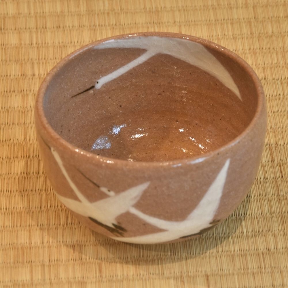 Angled top view of the Dancing Cranes matcha bowl showing its glossy brown interior and white crane decoration crossing the rim.