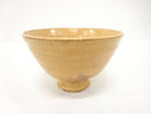 Front studio view of the Zuiho Ono Hagi chawan showing its gently flared Ido-style form, raised foot, and warm honey-amber glaze.