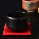 Kuro Raku Rikyu chawan matcha bowl with a deep black glaze displayed on a red cloth in a tea setting.