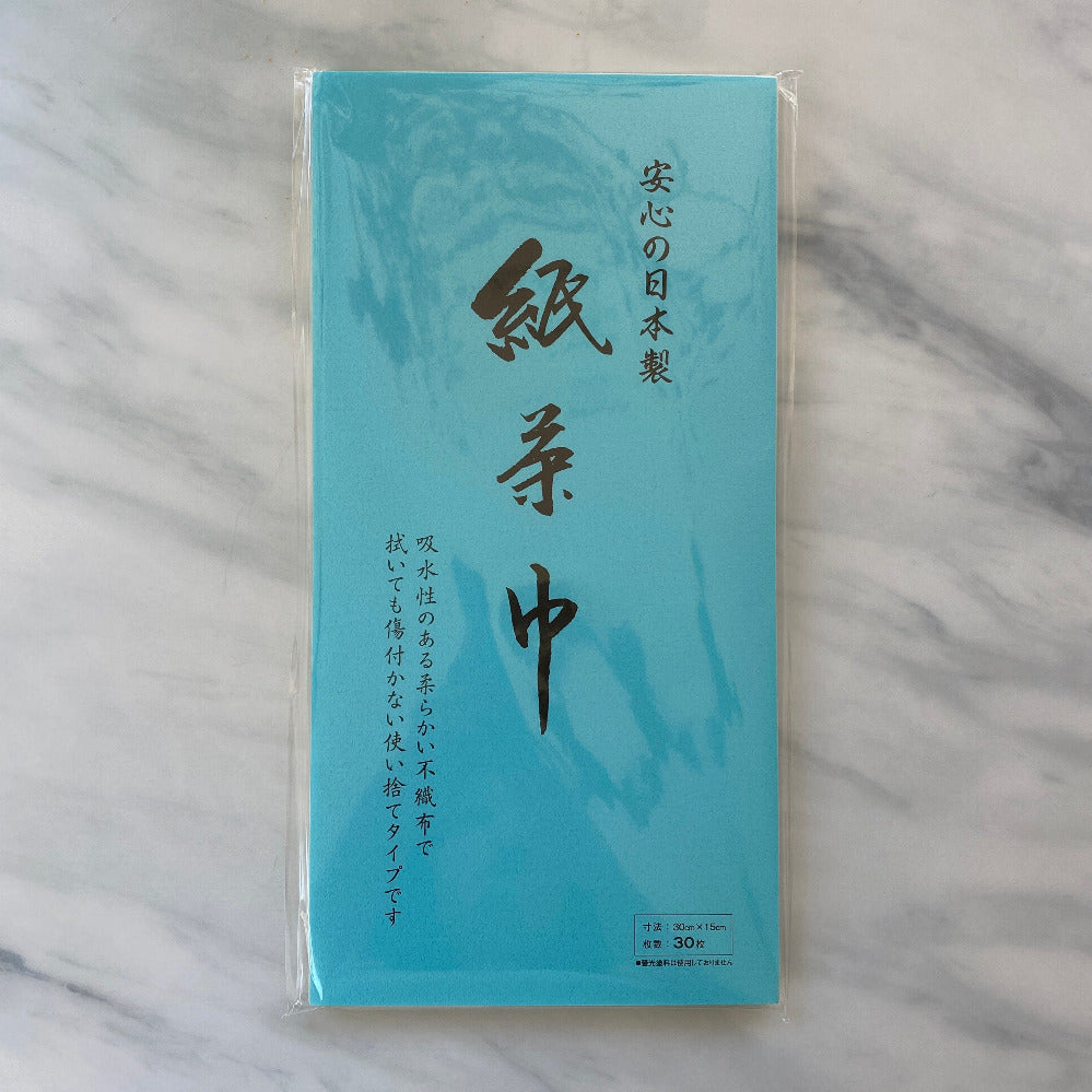 A blue paper chakin with Japanese characters printed in black, packaged in a clear plastic sleeve, placed on a marble surface.